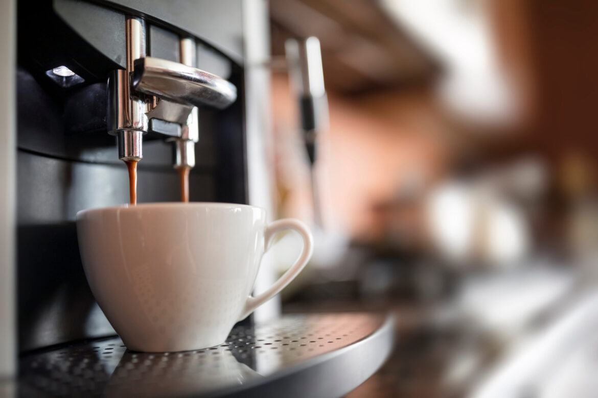 Espresso machine pouring coffee into a white ceramic cup on a metal drip tray.