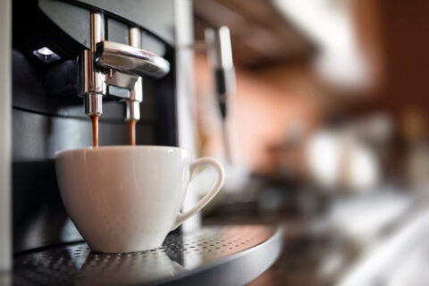 Espresso machine pouring coffee into a white ceramic cup on a metal drip tray.